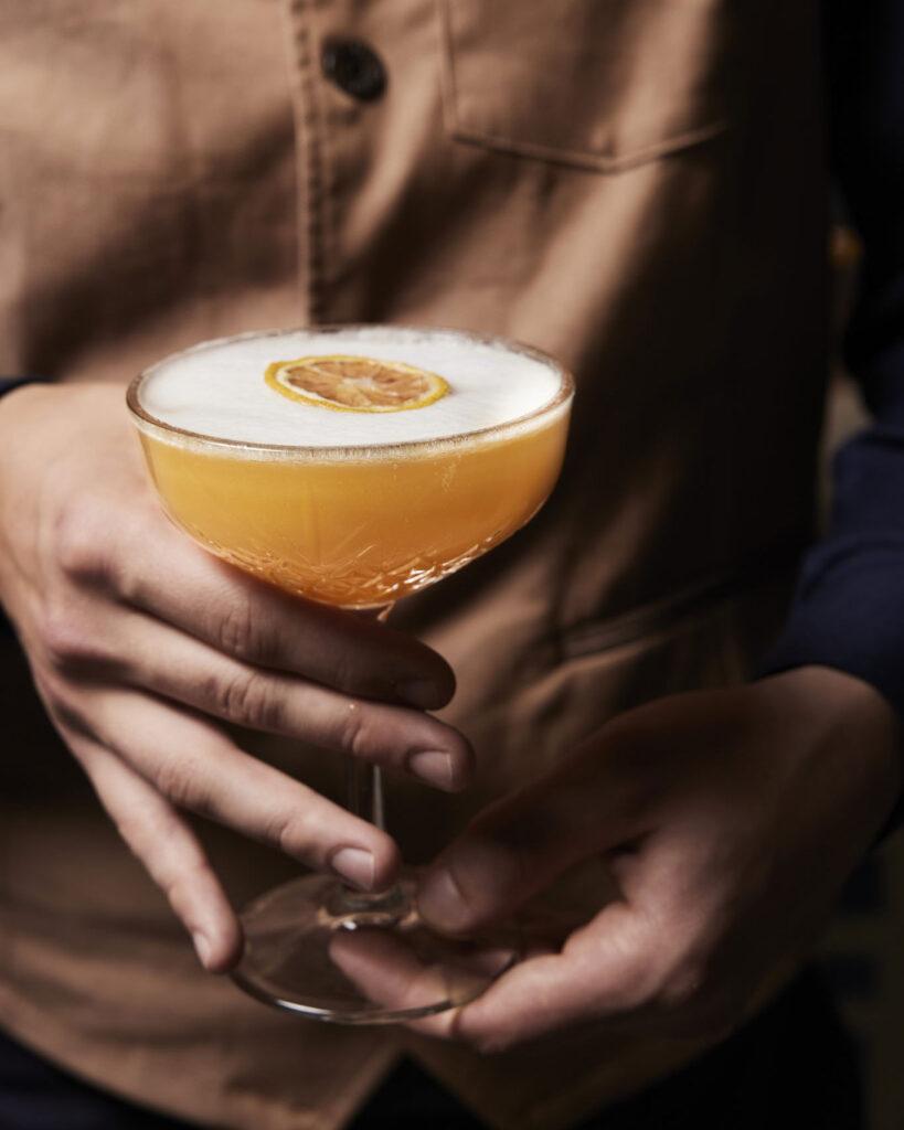 Hand hält eleganten Cocktail mit Zitrone in der Viertel Bar im Boutique Hotel Badhaus